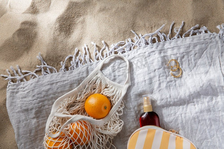 防晒沙滩摄影照片_休闲和暑假概念-沙滩毛毯上的橙子和防晒油袋子。沙滩毛毯上的一袋橙子和防晒油
