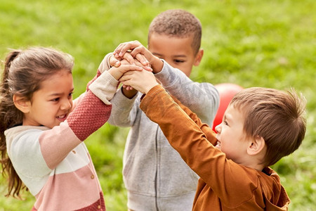 童年、休闲和人的概念-一群快乐的孩子在公园里玩耍和堆叠手。快乐的孩子们在公园里玩耍和握手