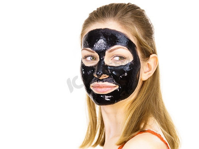 年轻女子脸上涂着化妆品，碳水化合物排毒黑脱口罩。水疗中心。护肤品..脸上戴着黑色口罩的女子