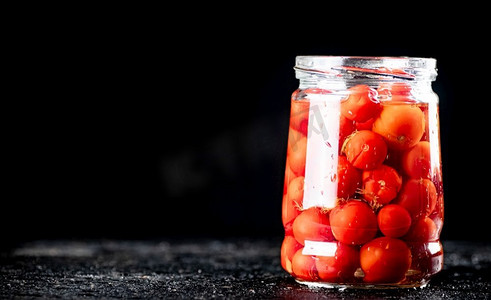 秘制泡菜摄影照片_桌子上的玻璃罐里的腌番茄。黑色背景。高质量的照片。桌子上的玻璃罐里的腌番茄。 