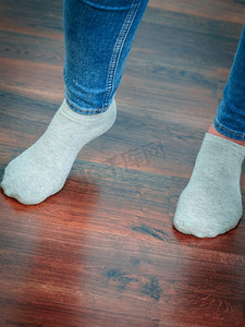 妇女脚站在木地板上穿着蓝色牛仔裤和轻袜子。无法辨认的女人穿着袜子