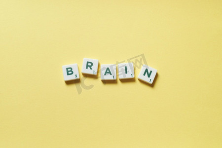 字黄色摄影照片_大脑词形成的拼字砖在黄色背景。大脑由拼字游戏形成。
