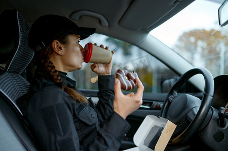 女警察在工作日吃午饭。女警官喝咖啡，在车里吃甜甜圈。女警官在工作日吃午餐