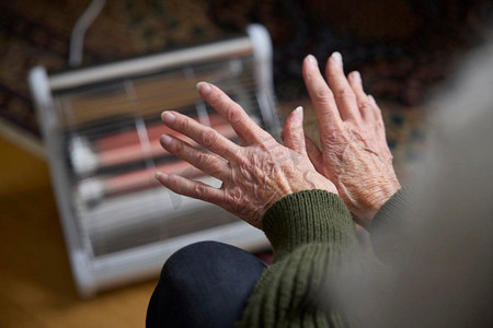 暖炉摄影照片_生活能源危机中的老年妇女在电暖炉上取暖的特写