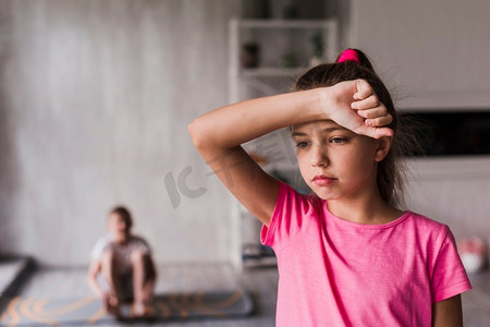 疲惫的女孩与她的手前额站在前面模糊的男孩背景