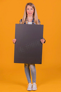 年轻女子拿着空白的黑色标语牌手反对橙色背景
