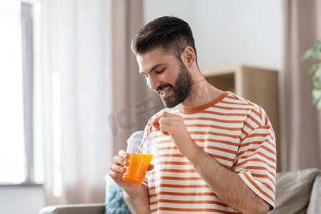 客户家里摄影照片_饮料和人的概念—微笑的男人喝橙汁与稻草在家里。微笑的男人在家里喝橙汁