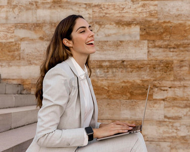 智能手表侧面摄影照片_侧面视图微笑的女商人与智能手表工作膝上型计算机户外