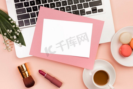 粉色漱口杯摄影照片_空白粉色纸笔记本电脑，带口红，化妆刷，咖啡杯，带杏仁办公桌