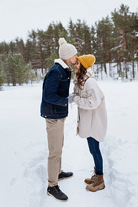 人，爱和休闲概念—快乐的男人亲吻女人额头在冬季森林。快乐的男人亲吻女人到前额在冬天