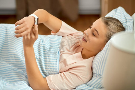 人，睡眠和休息的概念-微笑的女孩，戴着智能手表躺在家里的床上。微笑的女孩，戴着智能手表躺在家里的床上