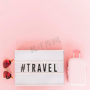 带有旅行文本的标签带太阳镜的灯箱迷你旅行包粉色背景