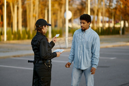 身穿黑色制服的女警察在街上检查男性路人的身份证件。女警察检查男性路人身份证件