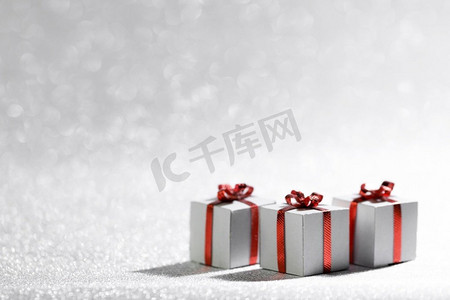 小装饰圣诞节礼物盒与红色丝带蝴蝶结在银闪光背景与复制空间。圣诞节礼物盒