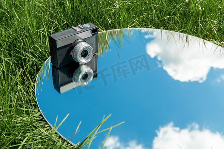 摄影和自然概念照相机和蓝天反射在草地的圆镜子。相机和天空反射在圆镜子在草