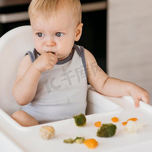 坐在高椅上吃蔬菜的可爱男婴