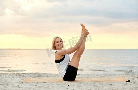 健身、运动和健康的生活方式概念—妇女做瑜伽船姿势在海滩超过日落。妇女做瑜伽船姿势在海滩