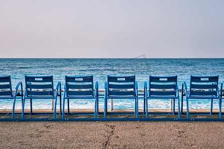 早上海滩上有著名的蓝色椅子长凳。很好，法国。法国尼斯海滩上著名的蓝色椅子