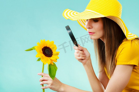 一位戴着黄色帽子的植物学家在蓝色背景上通过放大镜观察花卉
