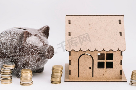 陶瓷piggybank与堆硬币在纸板房子白色背景附近