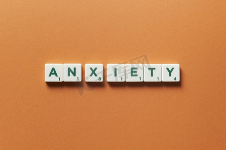 砖摄影照片_焦虑词形成的拼字砖橙色背景。恐慌发作和心理健康意识焦虑是由拼字游戏形成的。