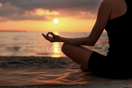 瑜伽，正念和冥想的概念-日落后，妇女在海滩上以莲花姿势冥想的特写。一名女子在海滩上摆出荷花姿势冥想
