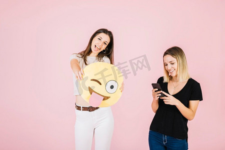 女人拿着眨眼的眼睛emoji靠近她的朋友使用手机