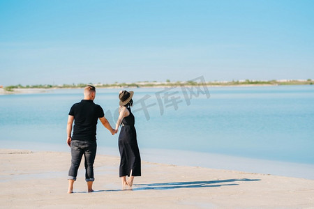 海水边摄影照片_一对年轻夫妇一个男人和一个女孩在蓝色的水边走在白色的沙滩上