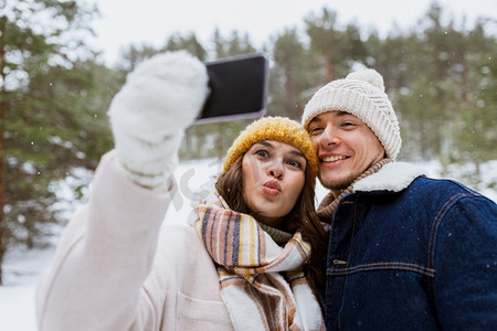 季节，技术和休闲概念—快乐的夫妇与智能手机采取自拍在冬季公园。夫妇与智能手机采取自拍在冬天