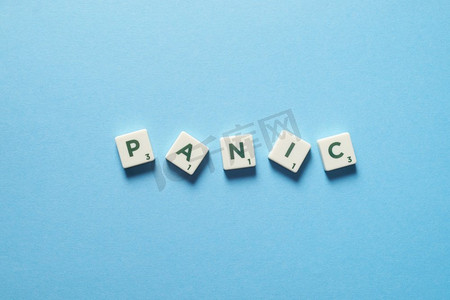 恐慌词形成的混乱拼字砖在蓝色背景。焦虑和心理健康意识由于乱涂乱画而产生的恐慌。
