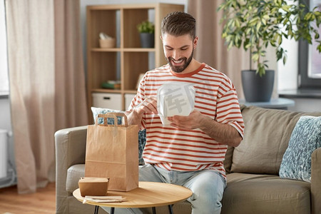 消费，吃和人的概念—微笑的男人打开外卖食品在纸袋在家里。微笑的男人在家里打开外卖食品
