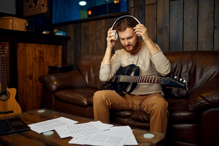 男子摘下耳机完成音乐课。他坐在家里的录音棚里吉他。男子脱下耳机完成音乐课
