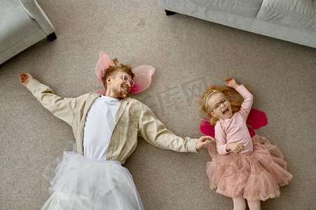 滑稽的穿着父亲和美丽的小女儿微笑的顶视图躺在地板上在家里。有趣的穿着父亲和女儿躺在地板上