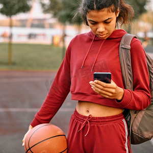 篮球框摄影照片_妇女拿着篮球户外检查她的电话2