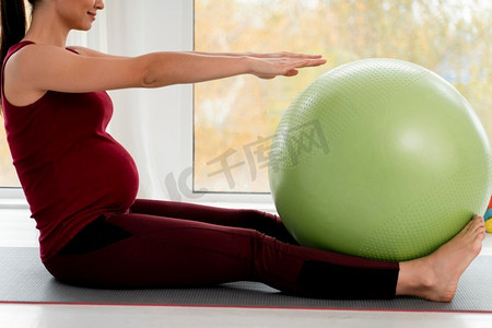 怀孕的年轻女子带着绿色健身球锻炼