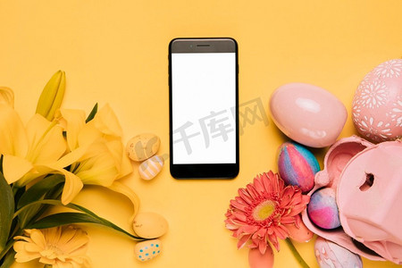 白色空白屏幕手机装饰百合非洲菊花五颜六色的复活节彩蛋黄色背景