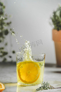 厨房挂壁摄影照片_自制的飞溅橙色柠檬水在玻璃与百里香在厨房桌子在墙壁和植物背景。清爽的夏季水果饮料。前视图。