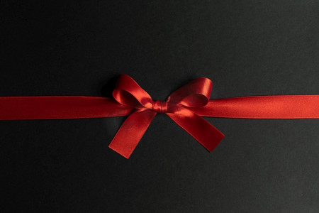 优雅的缎面红丝带蝴蝶结以黑色为背景。黑色上的红丝带蝴蝶结