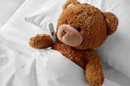 医学、保健和儿童概念-生病的泰迪熊玩具头，温度计躺在床上。生病的泰迪熊玩具头，床上有温度计