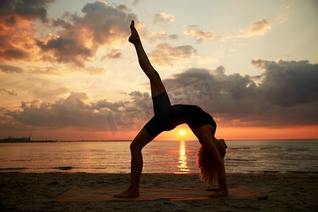 户外运动老外摄影照片_健身、运动和健康的生活方式概念—妇女做瑜伽桥姿势在日落的海滩。妇女做瑜伽桥姿势在海滩