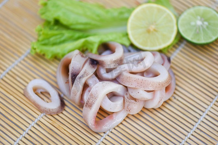 圈摄影照片_鱿鱼圈在木盘子，新鲜生鱿鱼与生菜蔬菜沙拉和柠檬酸橙