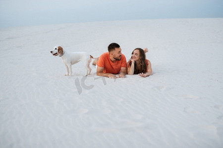 夏天衣服摄影照片_年轻夫妇橙色衣服与狗在沙漠白色的沙滩