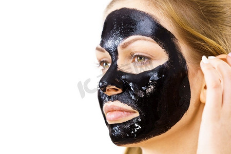 黑色口罩摄影照片_年轻女子脸上涂着化妆品，碳水化合物排毒黑脱口罩。水疗中心。护肤品..脸上戴着黑色口罩的女子