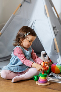 儿童玩玩具摄影照片_童年、休闲和人的概念-小女婴在家里玩玩具金字塔。快乐的女婴在家里玩玩具金字塔