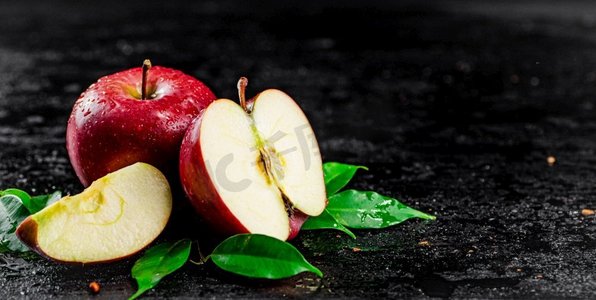 水果半个摄影照片_桌子上有半个和整个苹果，有叶子。黑色背景。高质量的照片。桌子上有半个和整个苹果，有叶子。