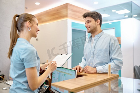 在现代诊所柜台，男访客与专业女接待员交谈。男子在诊所与专业接待员交谈