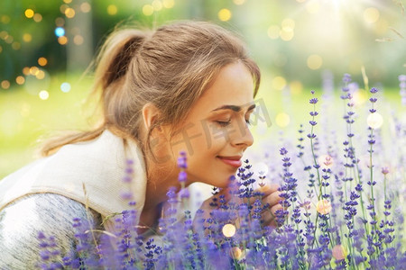 熏衣草摄影照片_园艺和人的概念—快乐的年轻妇女闻熏衣草花在夏季花园。年轻女子闻熏衣草花在花园