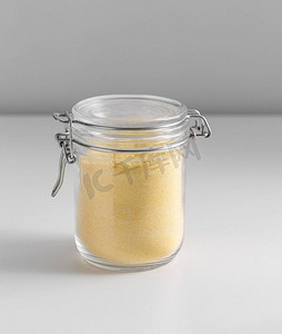 玉米粉摄影照片_食物储存，吃和烹饪概念—罐子与玉米粉在白色背景。关闭的罐子与玉米粉在白色桌子