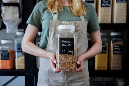 关闭销售助理在可持续的塑料免费全食店持有绿色扁豆容器