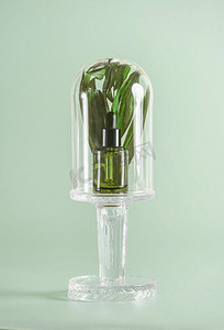 绿色血清瓶在玻璃钟罩与草药在浅绿色背景。天然化妆品。前视图